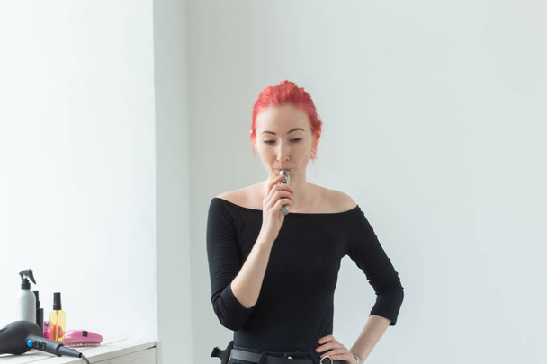 Youth and addiction concept - young red haired woman smoking vape near the window - Photo, image