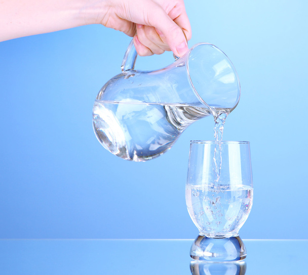 Glass pitcher of water and glass on blue background - Фото, зображення