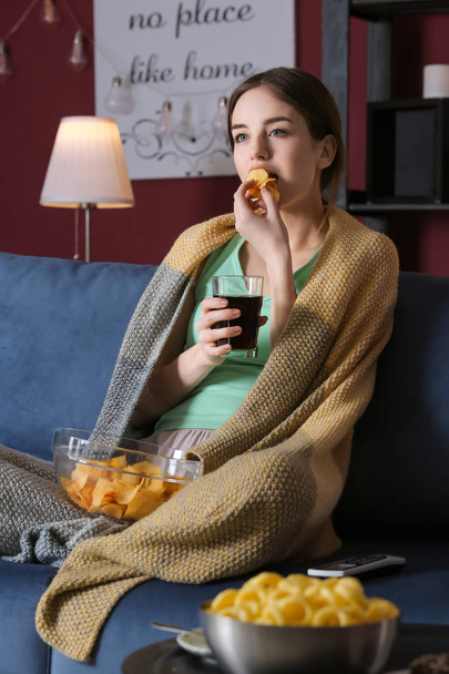 夜にテレビを見ている間に不健康な食べ物を食べる美しい若い女性 - 写真・画像