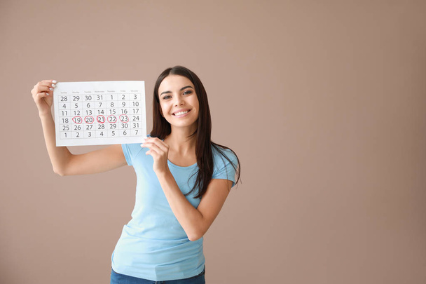 Young woman holding calendar with marked days of menstruation on color background - Photo, Image