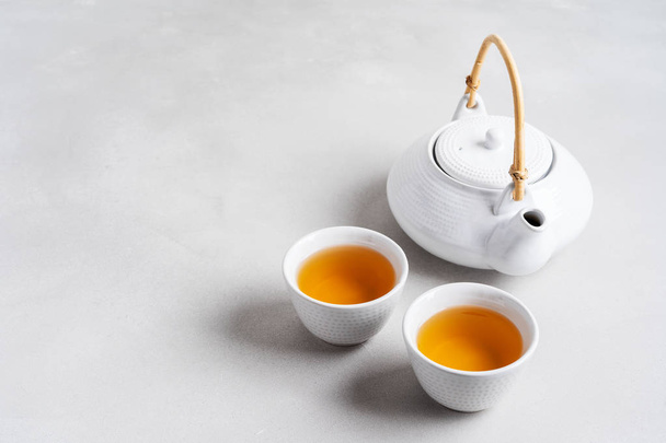 Λευκά φλιτζάνια τσάι και τσαγιέρα σε γκρίζο φόντο - Φωτογραφία, εικόνα