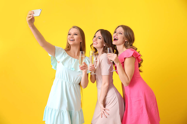 Όμορφες νεαρές γυναίκες με ποτήρια σαμπάνιας παίρνοντας selfie στο χρώμα φόντο - Φωτογραφία, εικόνα