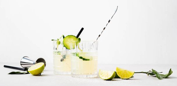Couple glasses of fresh cocktail with cucumber garnished with lime slices and micro greens on white background - Foto, imagen