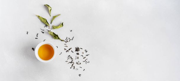 White cup of tea with green tea dry leaves on grey stone background - Foto, Imagem