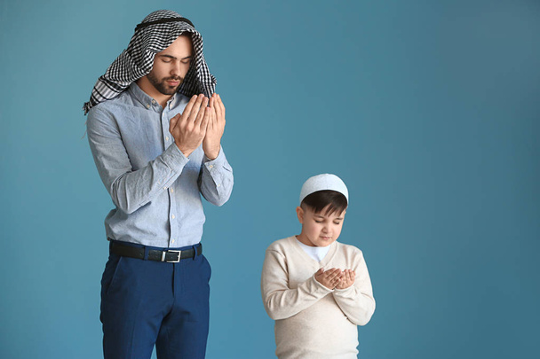 Young Muslim man and his son praying against color background - Fotoğraf, Görsel