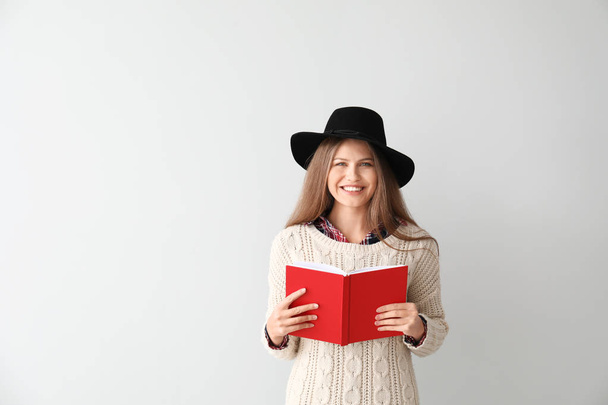 Mooie jonge vrouw met boek op lichte achtergrond - Foto, afbeelding