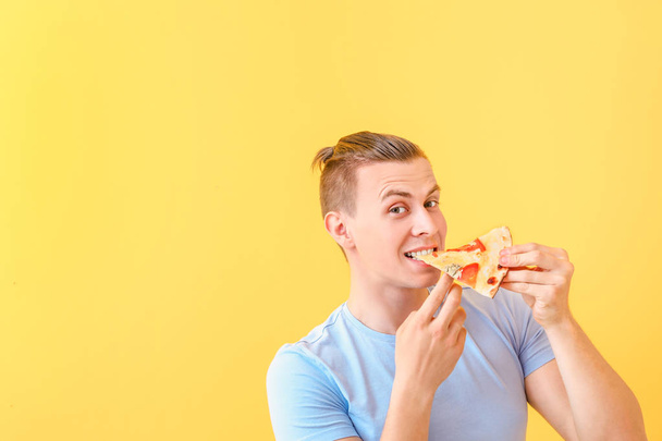 Hombre guapo comiendo sabrosa pizza en el fondo de color - Foto, imagen