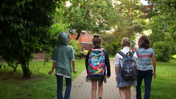 Beginn der Sommerferien, Ende des Schuljahres. Kinder laufen spaßig aus der Schule und wedeln mit Rucksäcken über den Köpfen - Filmmaterial, Video