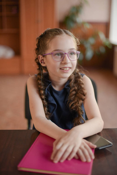 Koulutyttö istuu pöydässä oppikirjojen kanssa luokkahuoneessa. Tyttö sinisessä mekossa kanssa saparot
. - Valokuva, kuva