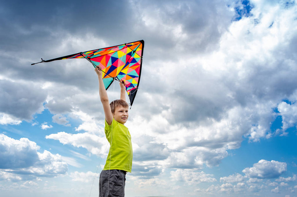 A boy with a colorful kite in his hands against the blue sky with clouds. Conceptual photography. A child in a yellow T-shirt - Фото, изображение
