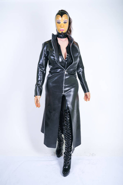 Plus size woman in latex suit and leather boots in thick heavy rubber raincoat on white background in Studio. hot fashionable adult girl posing in fetish clothes alone  - Фото, изображение