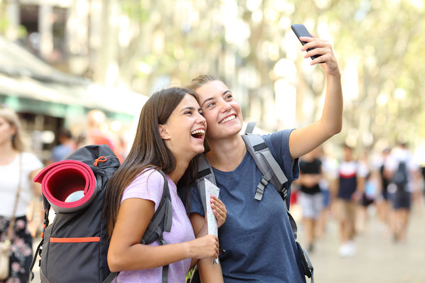 Two happy backpackers taking selfies in the street on vacation - Фото, изображение