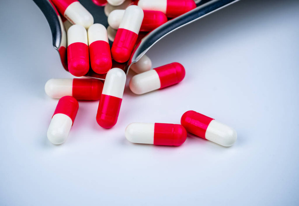 Red-white capsule pills on stainless steel drug tray and some on white table. Pharmacy drugstore background. Pharmaceutics concept. Pharmaceutical industry. Medicine in hospital. Global drug market. - 写真・画像