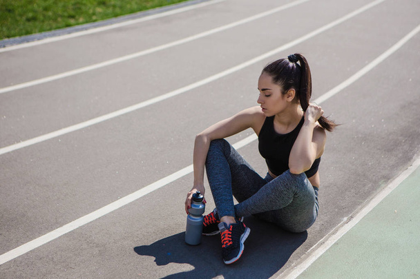 Mladá krásná tmavovlasá atletická dívka se potloukat ve sportu, ohřívala a provádí sportovní cvičení pro své zdraví a silné zdravé tělo na běžce na trati městské ulice - Fotografie, Obrázek