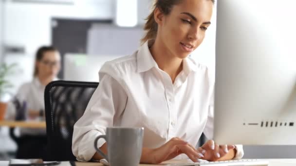 Young beautiful serious woman working in office using pc computer writing notes drinking coffee - Πλάνα, βίντεο