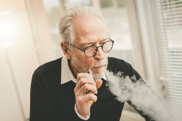 Senior man smoking electronic cigarette - Фото, изображение