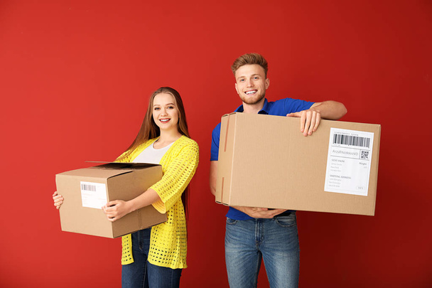 Young couple with cardboard boxes on color background - Fotó, kép