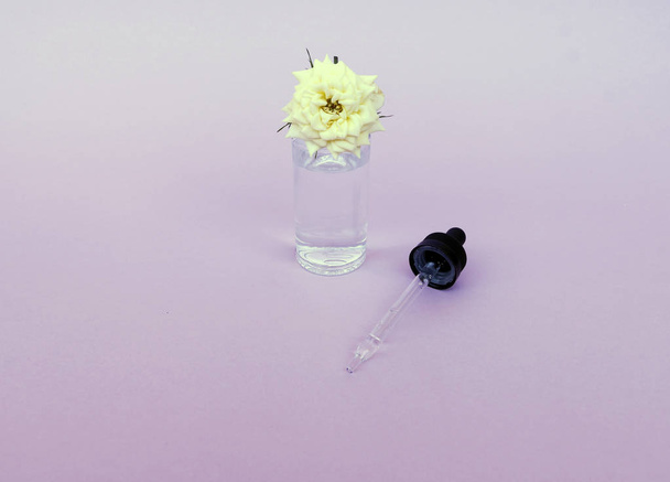 Glass bottle with pipette with oil or serum, with white rose flower on delicate background. Concept: organic bio cosmetics, vegetable oils, serum collagen, skin care - Photo, image