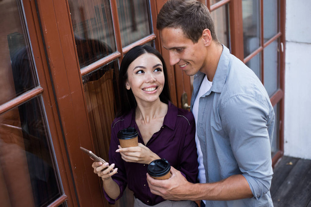 happy young couple holding disposable coffee cups and smartphone - 写真・画像