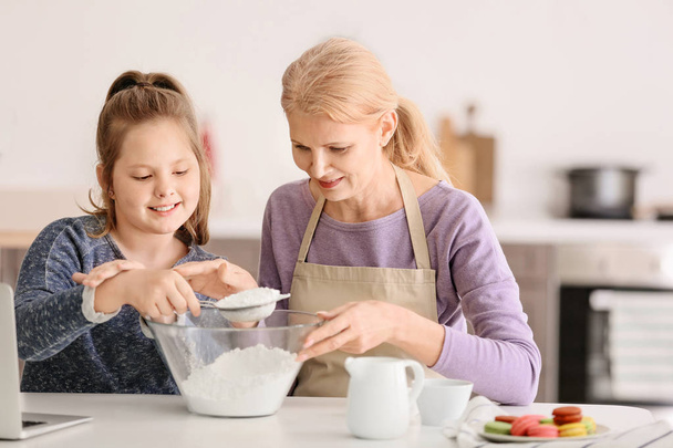 Mature woman and her cute granddaughter cooking in kitchen - Photo, Image
