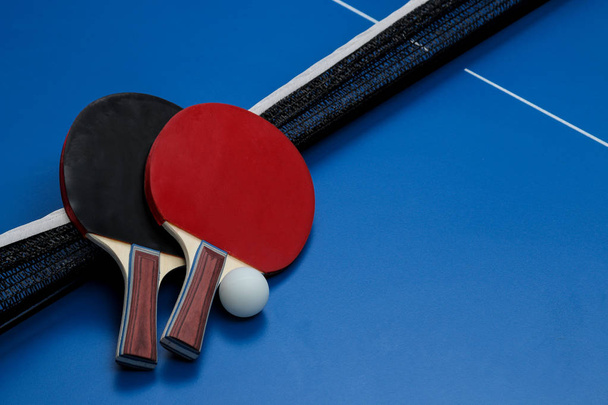 Dwa rakiety do ping-ponga. Rakiety do tenisa stołowego i piłka na niebieskim stole tenisowym - Zdjęcie, obraz