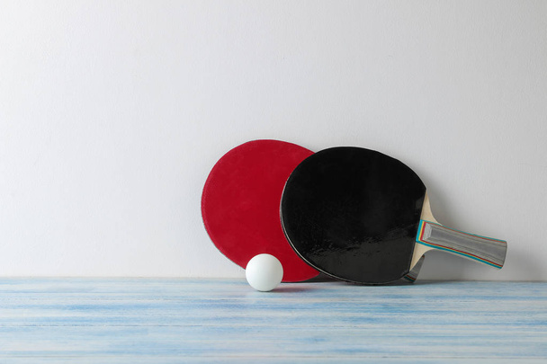 Twee ping pong rackets. Tafeltennis rackets en een bal op een blauwe houten tafel en tegen een muur - Foto, afbeelding