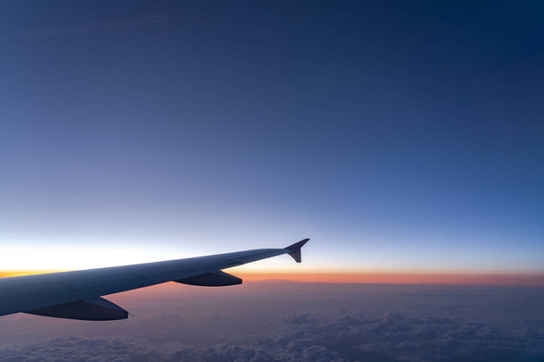 In de lucht, uitzicht op vliegtuig vleugel silhouet met donker blauwe hemel horizon en wolk achtergrond in zon opkomst tijd, bekeken vanuit vliegtuig venster - Foto, afbeelding