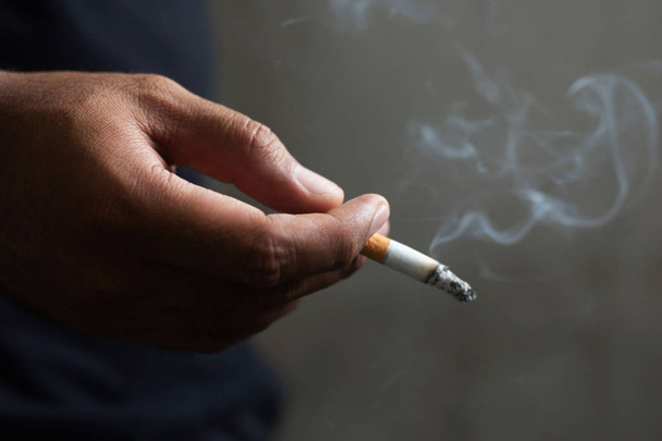 άνθρωπος που κρατά το κάπνισμα ένα τσιγάρο στο χέρι. Το τσιγάρο εξαπλώθηκε. σκούρο φόντο - Φωτογραφία, εικόνα