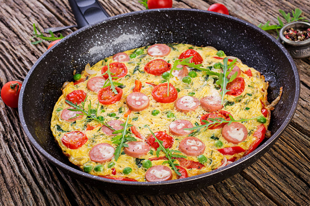 Omelette with tomatoes, sausage and green peas  in rustic style.  Frittata - italian omelet. - Фото, изображение