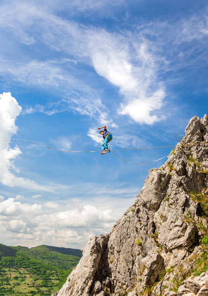 Jovem homem slackliner equilibrando em um slackline entre duas rochas. Destaque com uma bela paisagem natural por trás
 - Foto, Imagem
