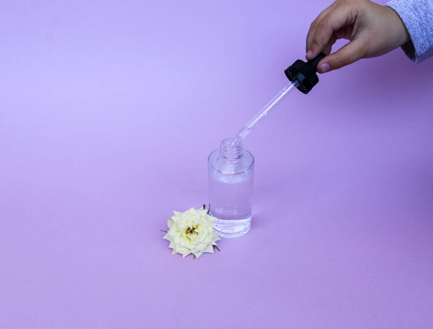 Glass bottle with pipette with oil or serum, with white rose flower on delicate background. Concept: organic bio cosmetics, vegetable oils, serum collagen, skin care - Zdjęcie, obraz
