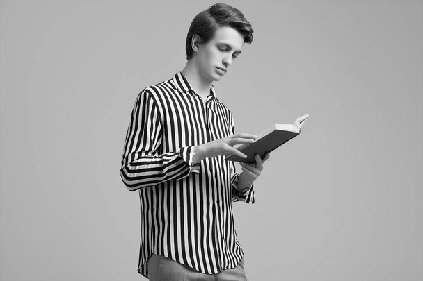 Młody przystojny mężczyzna w pasiasty koszula czytanie a książka na szary ciemny - Zdjęcie, obraz