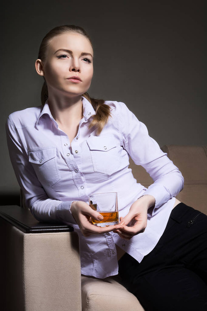 Beautiful girl sitting on the couch with a glass of whiskey - Foto, Imagem