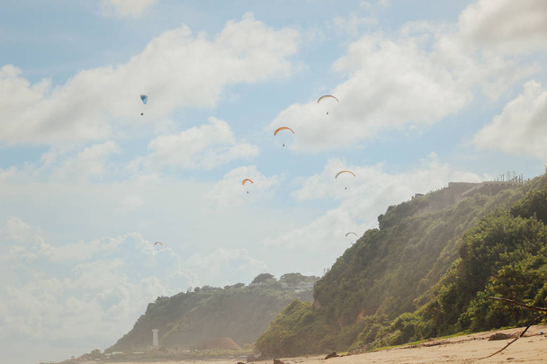 Paragliding in a Bali beach, Indonesia. Paraglider tandem flying over the beach, cliff, sea with blue water in bright sunny day - Φωτογραφία, εικόνα