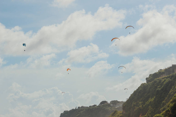 Paragliding in a Bali beach, Indonesia. Paraglider tandem flying over the beach, cliff, sea with blue water in bright sunny day - Фото, зображення