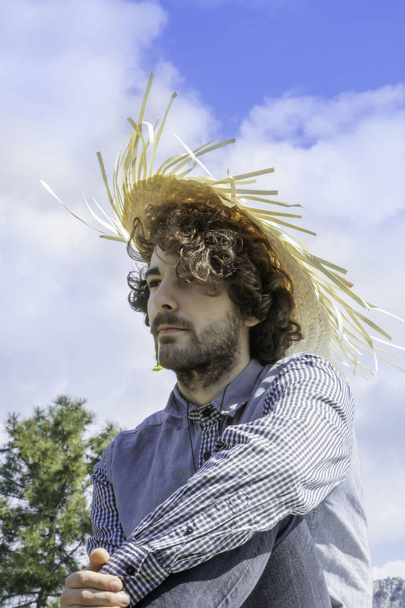 Young adult man looking away, brown curly hair with a West Indian straw hat on his head - Foto, Imagen
