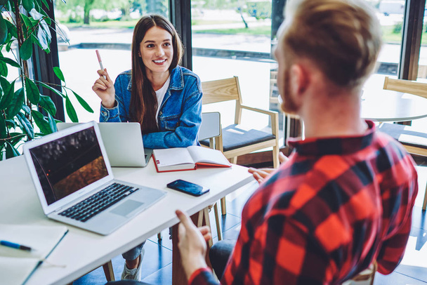 Positive male and female hipsters planning future event with friends from university using textbook and organiser application on laptops, happy freelance colleagues collaborating on netbooks - 写真・画像