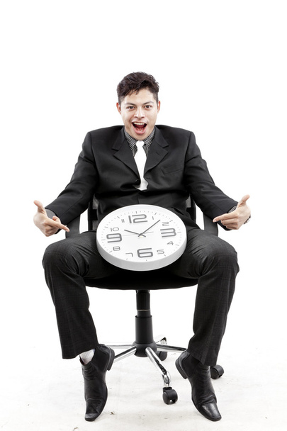 Porträt eines Geschäftsmannes, der sitzt und vor weißem Hintergrund eine Uhr zwischen sein Bein stellt - Foto, Bild