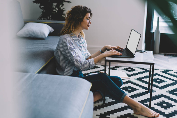 Caucasian woman typing text request on laptop computer for searching information on website for course work using home internet connection, hipster girl working remotely at netbook with blank screen - Photo, Image