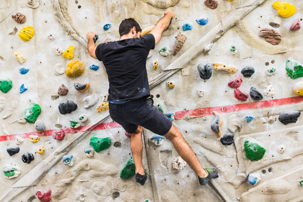 Hombre practicando escalada en roca en paredes artificiales en interiores. Activo
  - Foto, Imagen