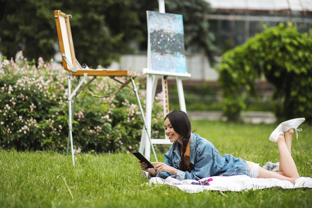 Young woman sitting with notebook and talking on mobile on grass. Woman studying outdoors with copy-book. Education, inspiration and remote working concept. - Photo, Image