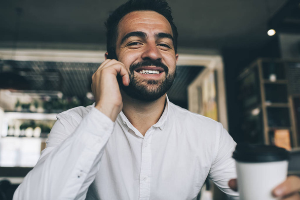 Portrait of happy accomplished male manager of coffee shop using public internet connection for making online smartphone conversation via communication application, concept of successful proud ceo - Foto, Bild