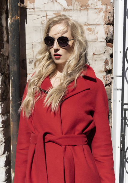 A beautiful blond girl wearing a red coat, sunglasses and gloves - Fotó, kép