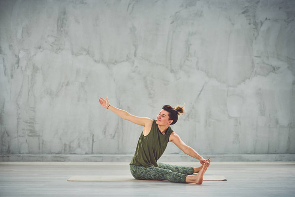 Красива кавказька брюнетка сидить на килимку з іншими ногами і робити вправи йоги. - Фото, зображення