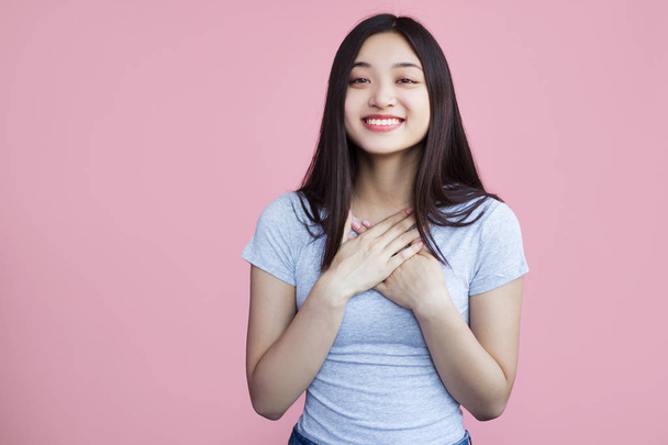 uśmiechnięta Azjatycka dziewczyna z rękami na klatce piersiowej na różowym tle - Zdjęcie, obraz