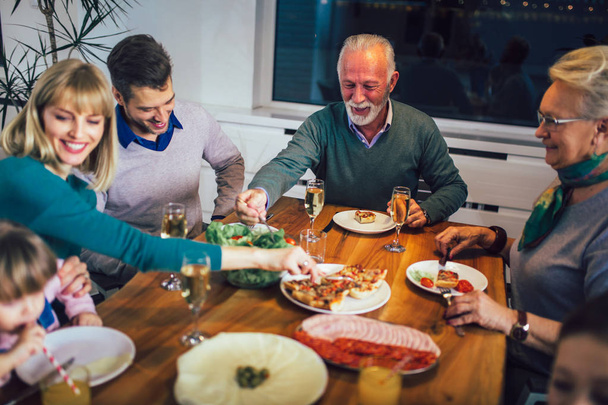 Família da multi geração que aprecia a refeição em torno da mesa em casa
 - Foto, Imagem
