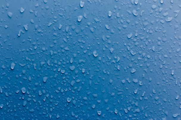 青い表面に透明な水滴が落ちる。抽象的な背景. - 写真・画像