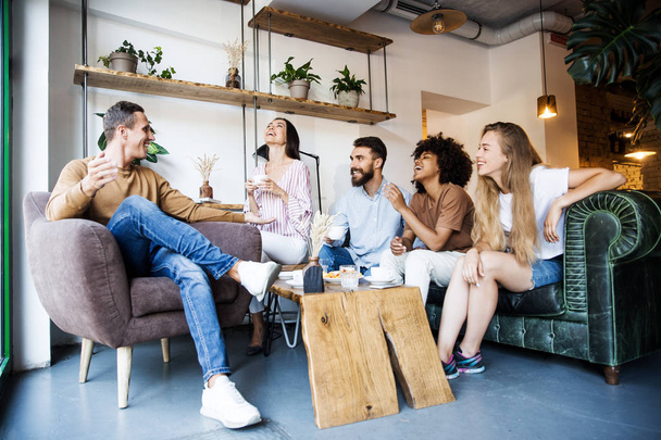 Grupo de jóvenes sentados en un café interior moderno, conversando y disfrutando juntos, tomando café y divirtiéndose
 - Foto, imagen