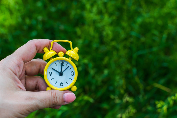 yellow alarm clock in a woman's hand on the background of nature - Photo, Image
