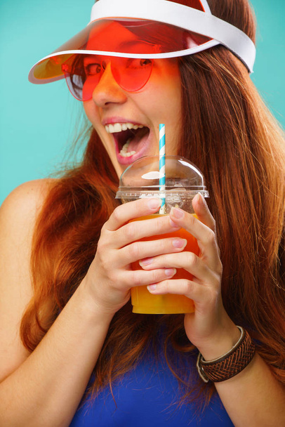 青い水着、帽子、サングラスを着た女性がカップからフルーツジュースを飲む - 写真・画像